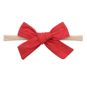 Dettaglio di un fiocco in tessuto rosso su una fascia elastica beige per neonati