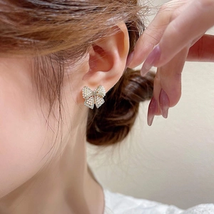 Elegant bow-shaped earrings with gold base, micro pearls, and cubic zirconia on a model