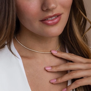 Close-up of a delicate gold tennis necklace with round cubic zirconia on a model