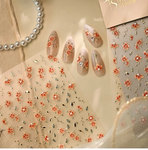 Detail of floral nail art stickers with orange flowers and embossed gold leaf patterns
