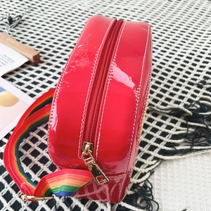 Detail of red patent leather crossbody bag featuring a vibrant rainbow woven shoulder strap