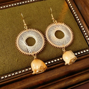 Detail of bohemian round woven earrings with yellow dried flower buds on green fabric