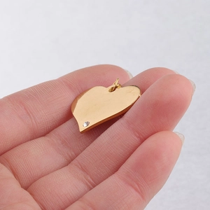 Detailed view of a golden heart pendant with a small inlaid diamond held by a hand