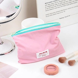 Pink minimalist makeup bag with turquoise zipper and white woven label on vanity table