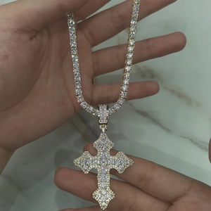 Détail d'un pendentif croix dorée en zircone avec chaîne assortie tenu à la main délicate