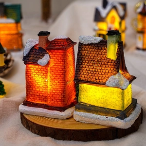 Close-up of glowing resin Christmas house ornaments with warm LED light and snow texture