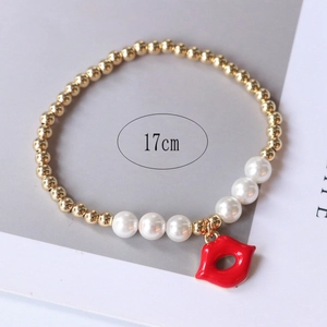Detail of a 17cm stretch bracelet with gold beads, pearls, and a red lip pendant charm