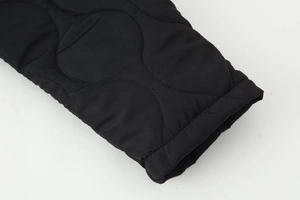 Gros plan sur le motif matelassé ondulé et le poignet élastique d'une veste noire