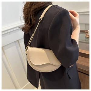 Beige crescent moon shoulder bag with gold chain strap worn over a black blazer