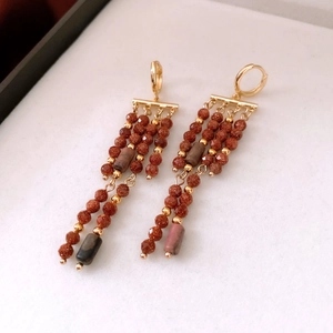 Vue macro de boucles d'oreilles vintage en grès brun-rouge avec franges dorées
