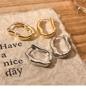 Close-up of irregular wave-shaped chunky hoop earrings in gold and silver finishes