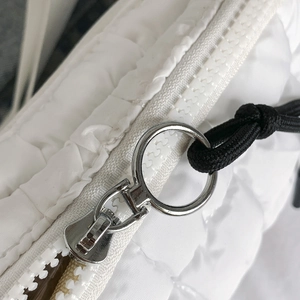 Detail of white quilted fabric with silver ring zipper and black drawstring puller