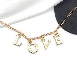 Goldene LOVE Buchstaben Anhänger Halskette auf Seidenstoff und schwarzem Hintergrund