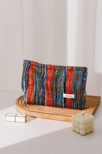 Detail of colorful bohemian striped knitted pouch with H&R brand label on a wooden stand
