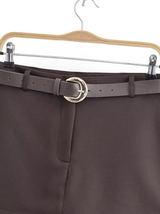 Detail of dark brown tailored trousers with slim belt and golden crescent metal buckle