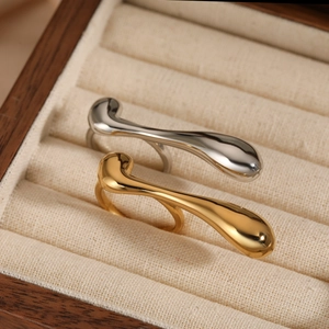 Irregular droplet shaped open rings in gold and silver finish on a wooden jewelry box
