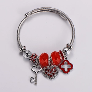 Detailed view of silver charm bracelet with red beads, crystal heart and key pendant