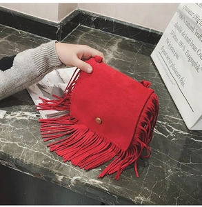 Detail of red suede crossbody bag featuring long bohemian tassels and metal snap button