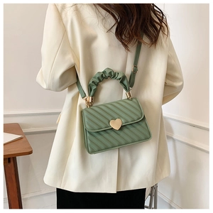 Detail of light green quilted handbag featuring a gold heart clasp and pleated top handle