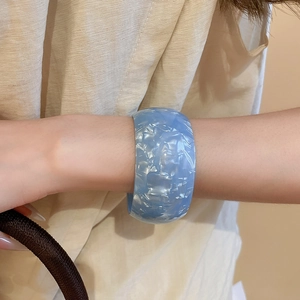 Blue acrylic open bangle featuring marble texture and iridescent finish worn on wrist