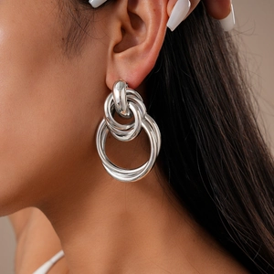 Close-up of a model wearing silver metallic knot earrings with layered geometric hoops