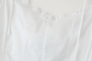 Detail of white spaghetti strap dress featuring ruffled neckline and stitching details