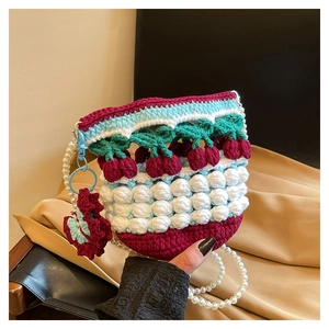 Close-up of handmade knit bucket bag with cherry charms and elegant white pearl strap