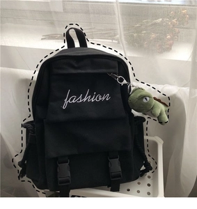 Close-up of black canvas backpack featuring fashion embroidery and a green dinosaur charm