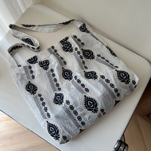 Detail of linen tote bag featuring black folk-style plant embroidery and textured fabric