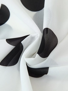 Makroaufnahme von weißem Chiffonstoff mit schwarzen Punkten und glatter Textilstruktur