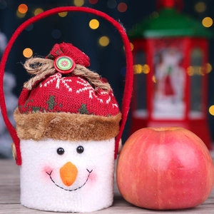Plush snowman gift bag with red handle and knitted closure next to a red apple decoration
