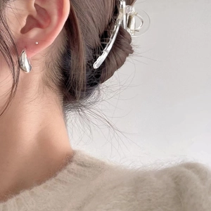 Close-up of a sleek silver teardrop earring worn by a model with a clear hair claw clip