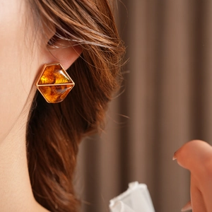Close-up of geometric hexagonal amber resin earrings worn by a model in soft lighting