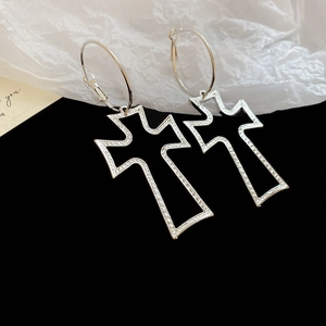 Detailed view of silver hoop earrings featuring textured hollow cross pendants on black velvet