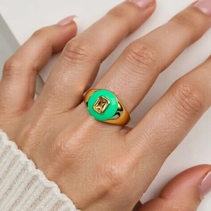 Close-up of a wide gold signet ring featuring green enamel and a clear square zircon stone
