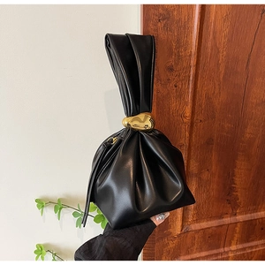 Detailed view of black pleated bucket bag featuring a large gold pebble metal accent
