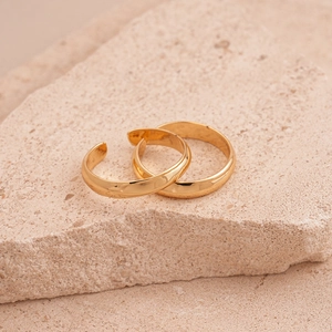 Detailed shot of gold geometric cuff rings on a beige textured stone block background