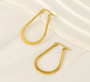 Macro detail of polished gold U-shaped earrings on elegant cream satin fabric