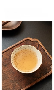 Detail of petal-shaped ceramic tea cup with rustic speckled glaze on wooden tray