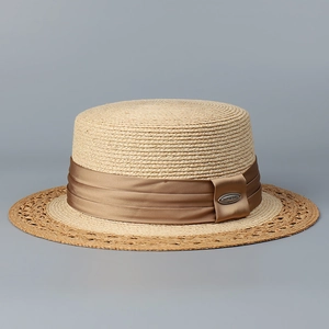 Detail of a beige boater hat with a brown silk ribbon and decorative metal brand plate