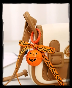 Close-up of orange pumpkin bell charm and leopard bow on a brown leather shoulder bag