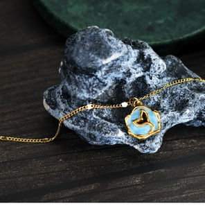 Macro view of blue enamel whale tail pendant on gold chain over rustic grey rock