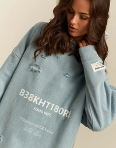 Detail of light blue washed hoodie featuring distressed holes and FOMO DEPT. lettering