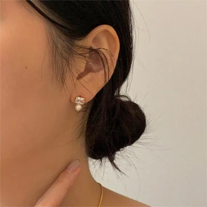 Detail of square zircon and pearl earring worn on the ear showing elegant gold plating