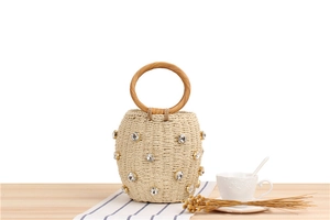 Macro detail of hand-woven straw bucket bag with crystal accents and round wooden handle