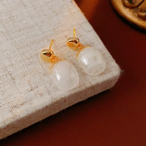 Detailed shot of 18K gold plated resin earrings on beige linen with soft lighting