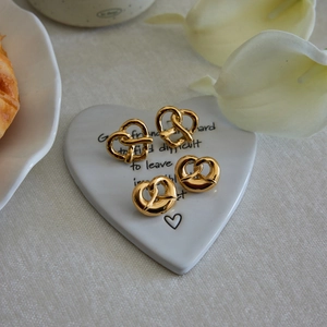 Golden heart-shaped knot earrings on a decorative white ceramic tray with flowers