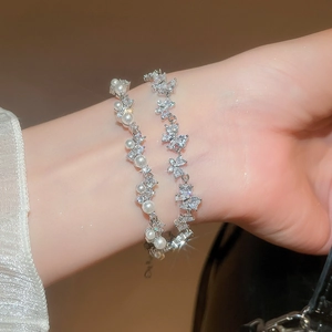 Detail of layered silver bracelets featuring butterfly zircons and white pearls on wrist