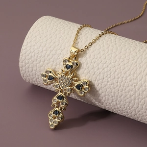 Golden cross necklace with blue heart zircon stones on a white textured leather roll