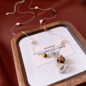 Detail of tiger eye and pearl beaded necklace with a carousel horse pendant on a tray